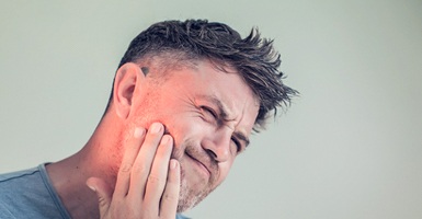 A middle-aged man holds his jaw while cringing in pain