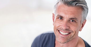 Grey haired man with a grey shirt smiling