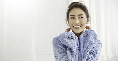 A young woman wearing a blue sweater smiles after wearing a customized nightguard that is designed to keep her from grinding her teeth in Odessa