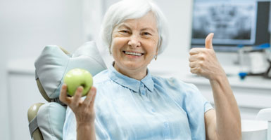 elderly woman giving a thumbs-up and holding a green apple