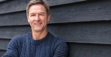 Man in a blue sweater smiling in front of a dark background