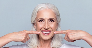 Woman in a white shirt pointing to her smile