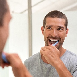 Man smiling while brushing his teeth in the mirror