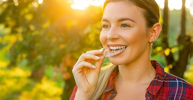 Woman smiling outside putting in Invisalign in Odessa, TX