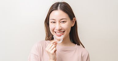 Woman in light pink shirt putting in Invisalign in Odessa, TX
