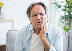 Older man sitting in chair and rubbing jaw in pain